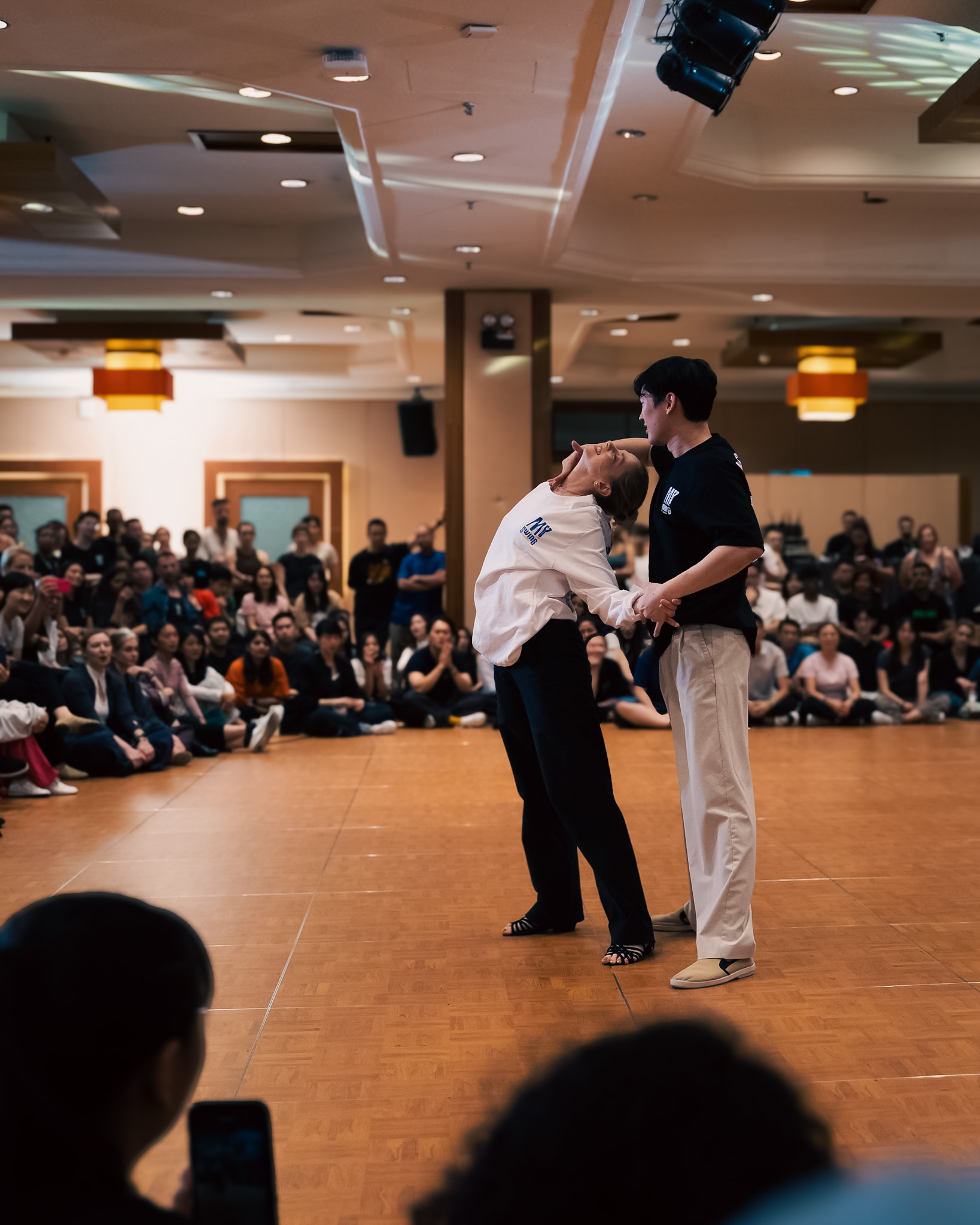 A couple dances at center floor as the audience watches.