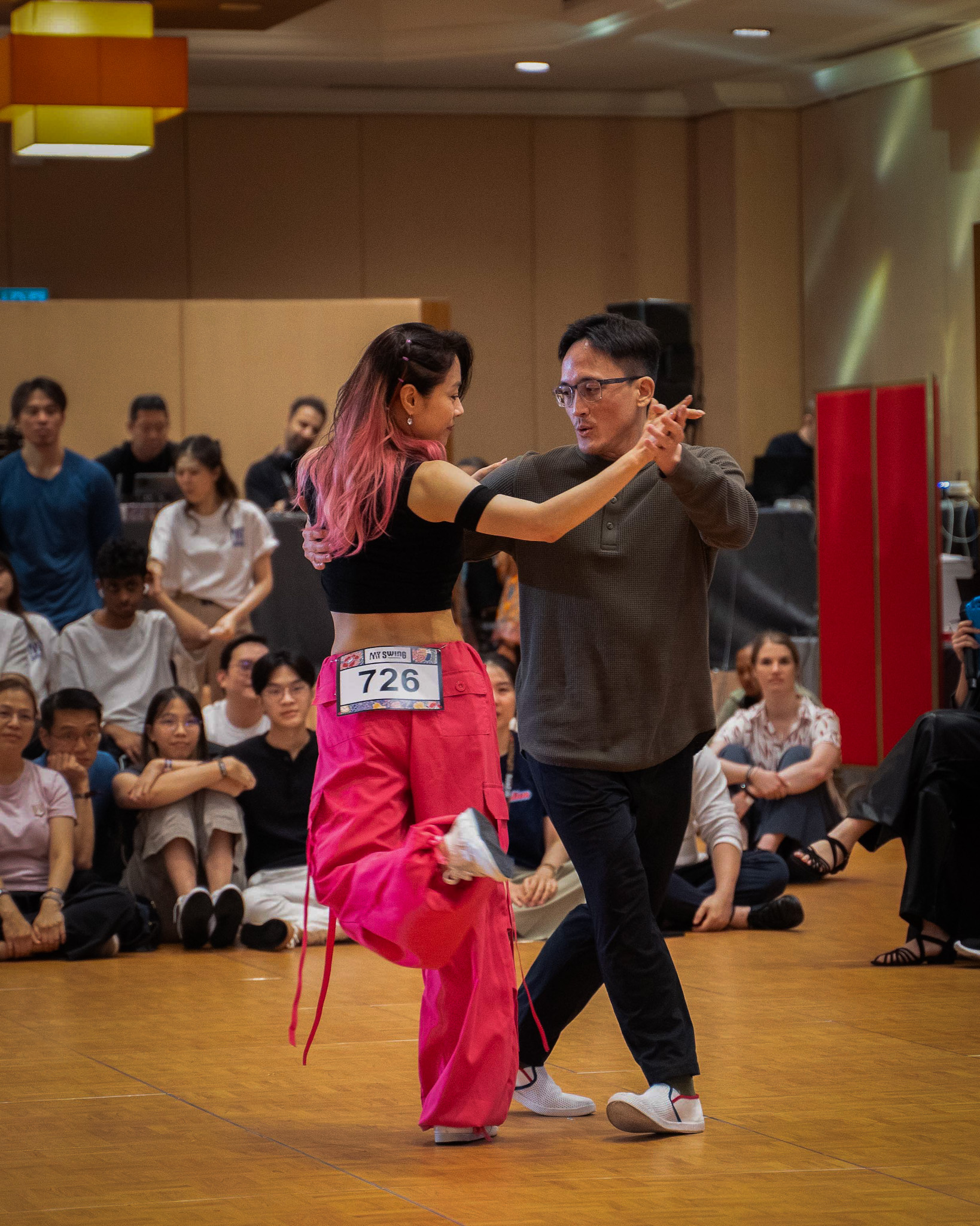 Partners dance together in bright pink and dark outfits.