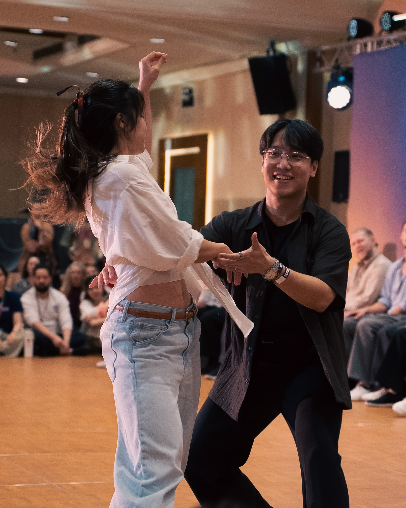 Partners smile through a turn near the edge of the floor.