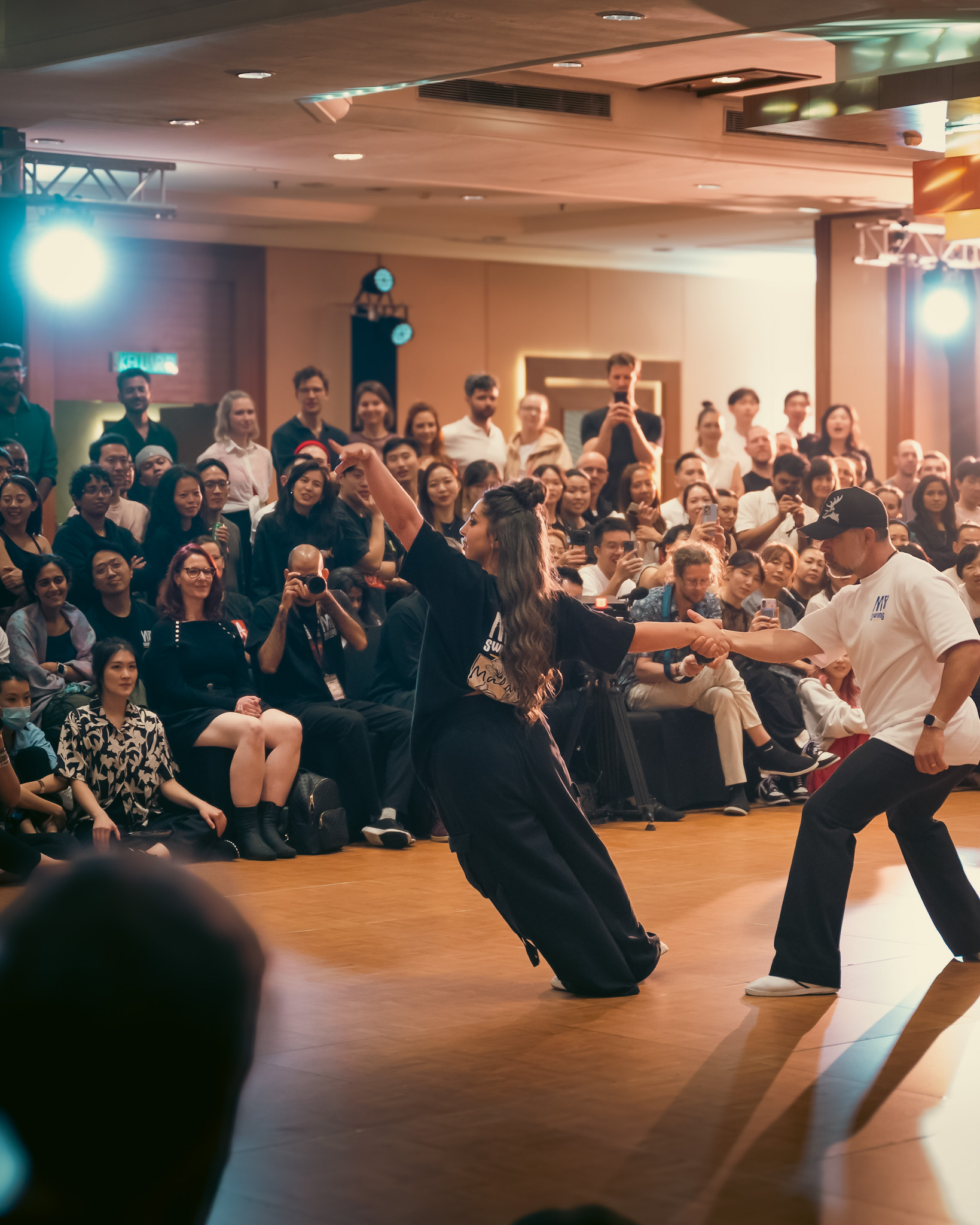 Performers move across the floor as a packed audience watches.