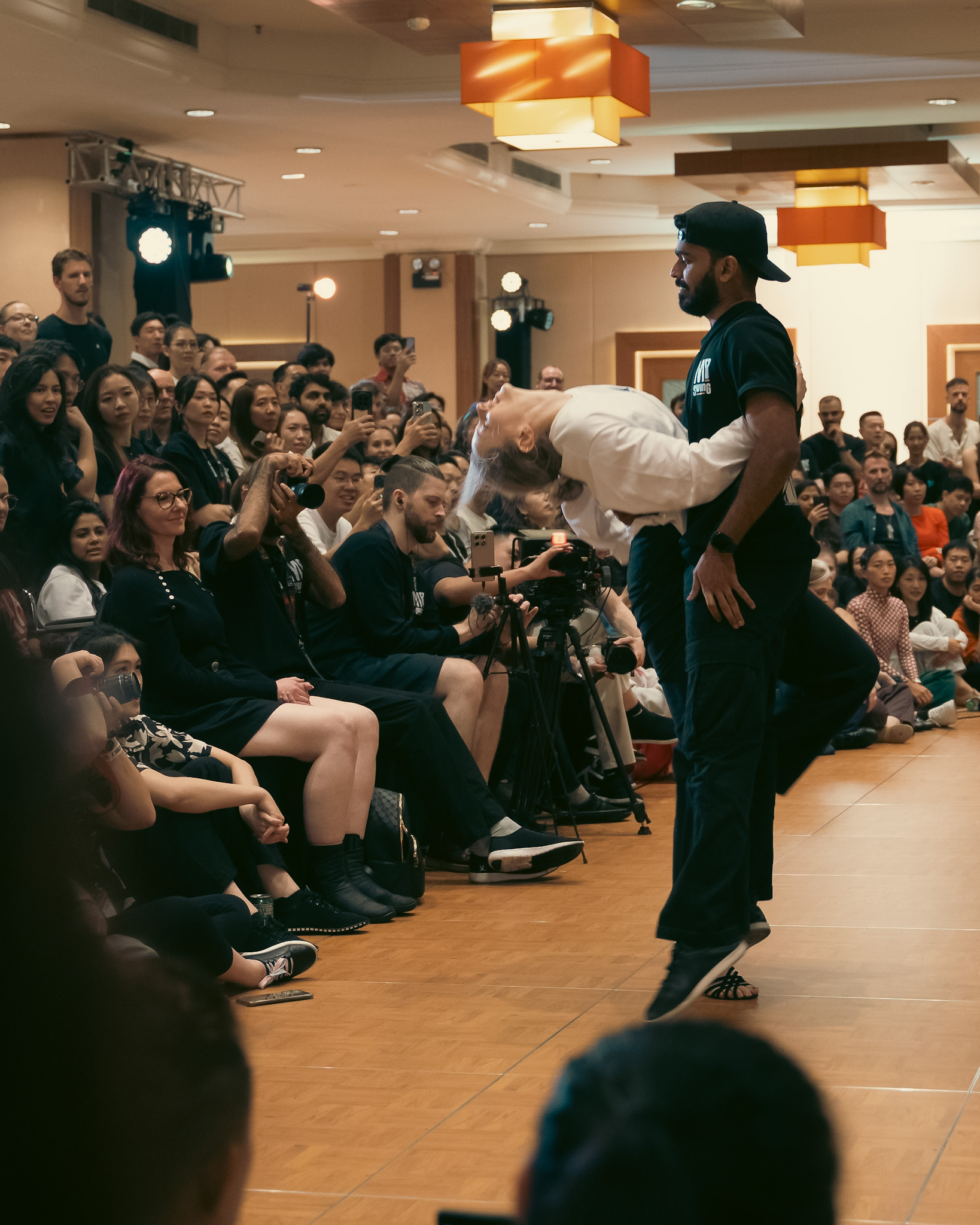 A partner carries another dancer across the floor.
