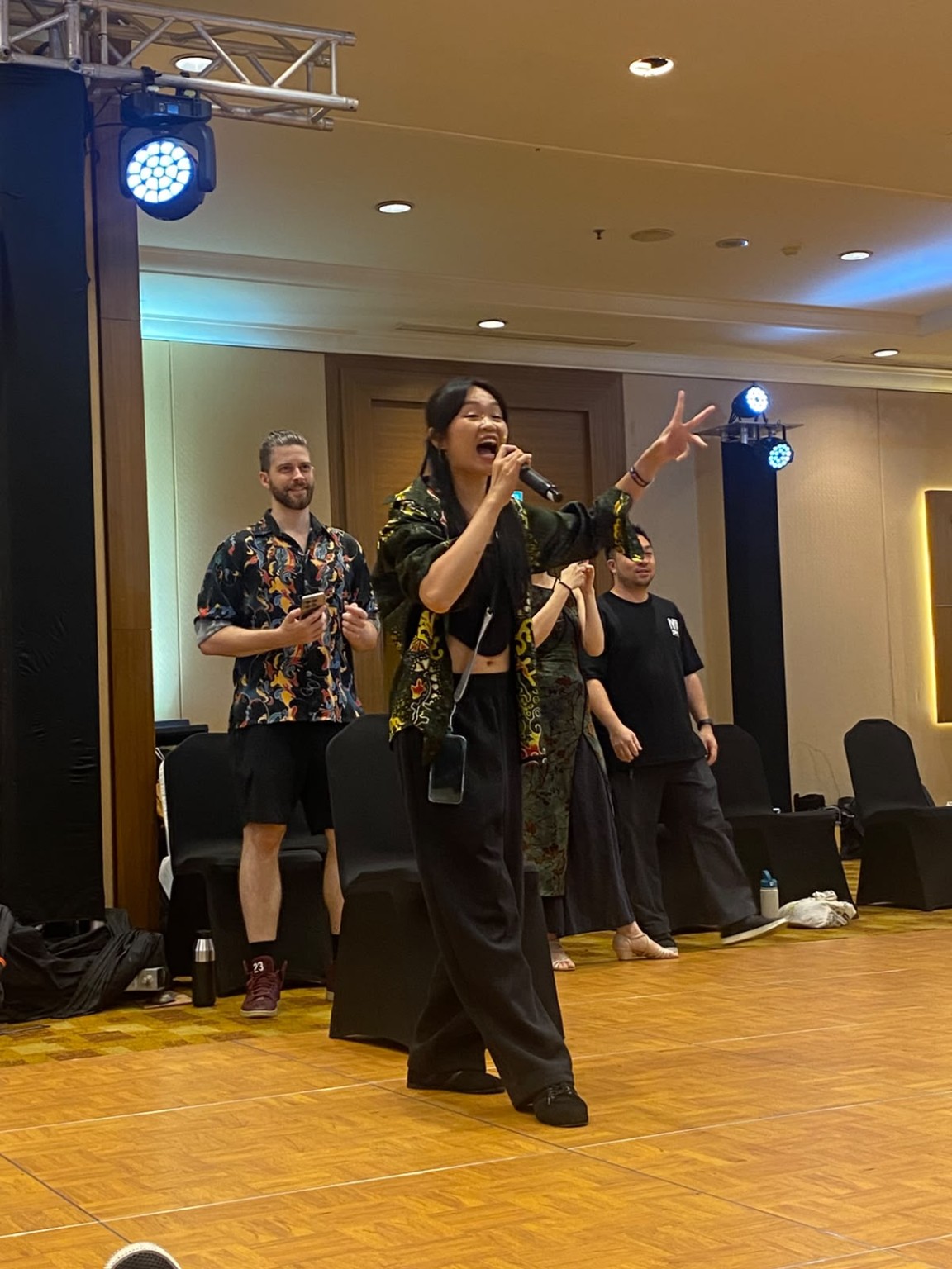 A person holding a microphone gestures in the ballroom at MY Swing 2026.